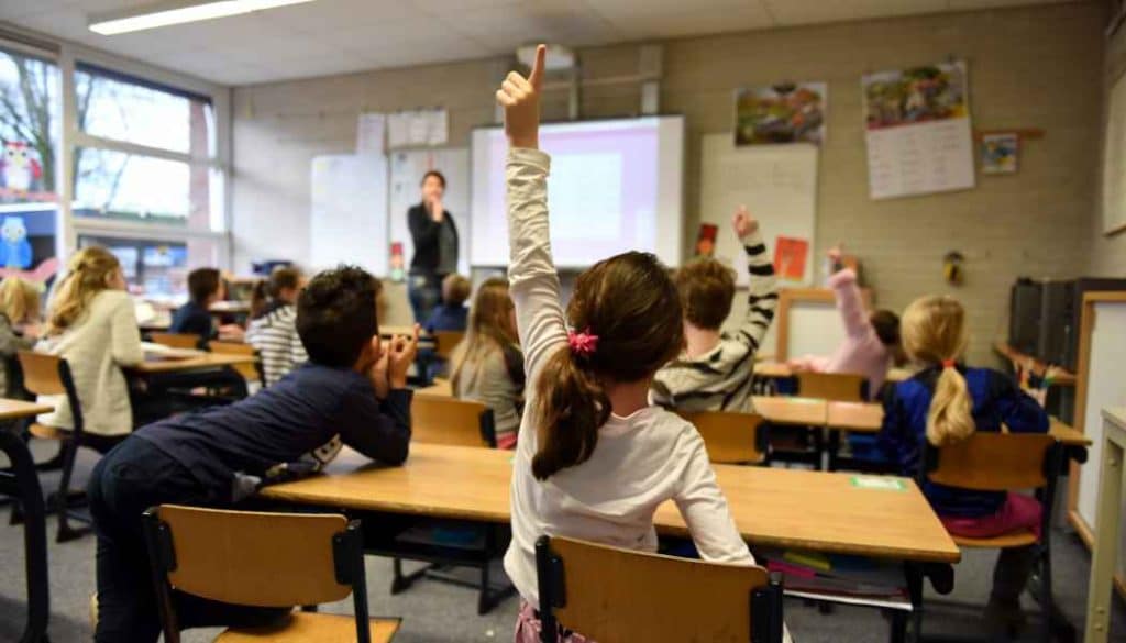 Inside view of a classroom where children are engaged in learning, with three hands raised, ready to participate.