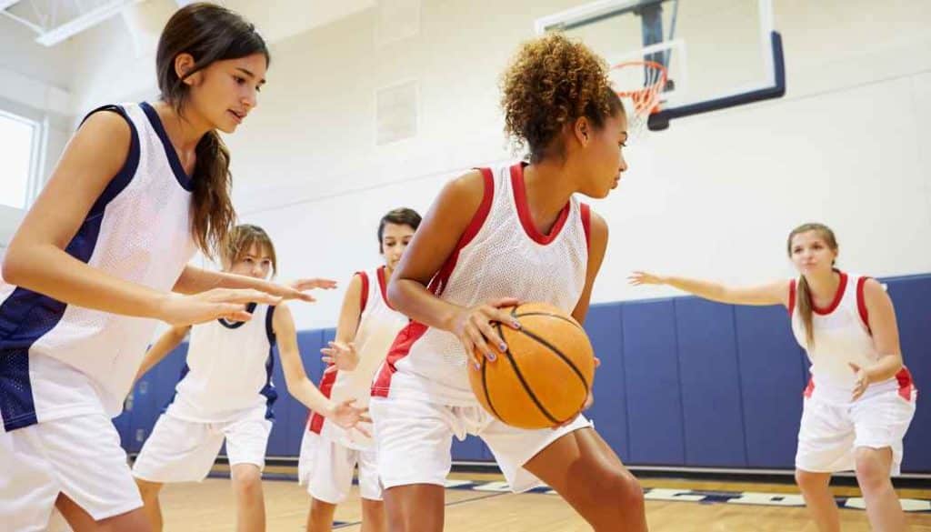 Five girls in gym uniforms playing basketball, highlighting extracurricular opportunities at the best schools for military families during a PCS move.