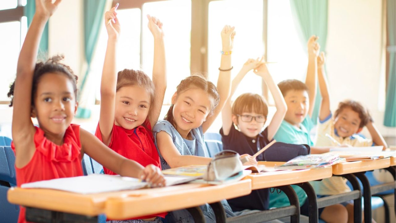 Classroom scene with six children raising their hands, representing the best schools for military families during a PCS move.
